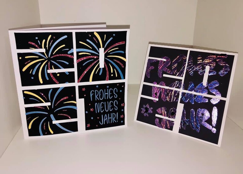 Puede incluir: Dos tarjetas negras con borde blanco. La tarjeta de la izquierda tiene una cuadr&iacute;cula de cuatro cuadrados con ilustraciones de fuegos artificiales en cada cuadrado. La tarjeta de la derecha tiene una cuadr&iacute;cula de cuatro cuadrados con el texto "Frohes Neues Jahr!" en cada cuadrado. El texto est&aacute; en una fuente brillante e iridiscente.