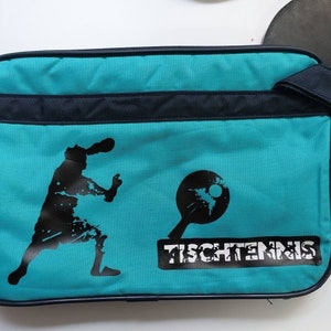 May include: A teal blue table tennis bag with a black silhouette of a player and a table tennis paddle. The bag has a black zipper and a black strap. The text "TISCHTENNIS" is printed in black on the bag.