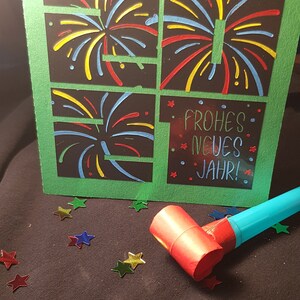Puede incluir: Una tarjeta verde con fondo negro y dise&ntilde;os de fuegos artificiales coloridos. La tarjeta dice "Frohes Neues Jahr!" que es alem&aacute;n para "&iexcl;Feliz A&ntilde;o Nuevo!"