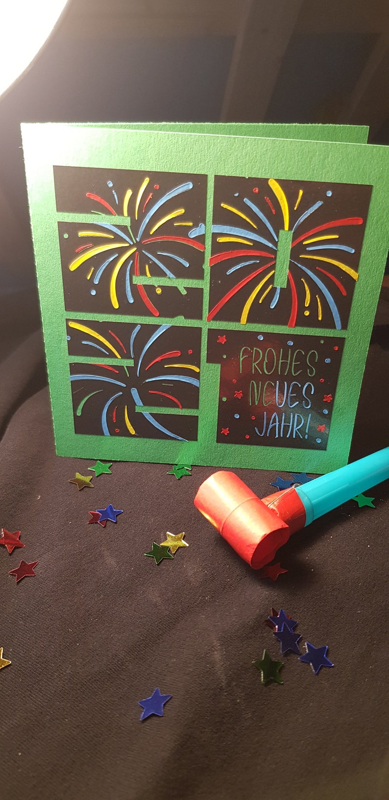 Puede incluir: Una tarjeta verde con fondo negro y dise&ntilde;os de fuegos artificiales coloridos. La tarjeta dice "Frohes Neues Jahr!" que es alem&aacute;n para "&iexcl;Feliz A&ntilde;o Nuevo!"