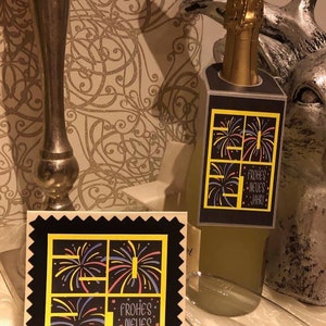 Puede incluir: Una tarjeta negra y amarilla con un dise&ntilde;o festivo de fuegos artificiales y el texto "Frohes Neues Jahr!" La tarjeta est&aacute; sobre una mesa junto a una botella de champ&aacute;n.