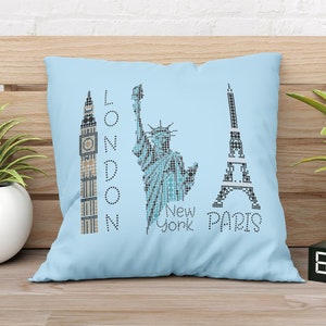 Könnte beinhalten: Ein hellblaues Kissen mit einem Design aus Eiffelturm, Freiheitsstatue und Big Ben. Der Text "LONDON", "NEW YORK" und "PARIS" ist auf dem Kissen aufgedruckt.