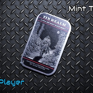 May include: A black and white illustration of a person walking on a path in a forest. The illustration is on a metal tin with the text "Tin Realm: A Solo Journey Back Home" and "Designed & Illustrated by Jason Glover".