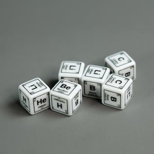 May include: Six white dice with black lettering showing the chemical symbols for the elements Helium, Beryllium, Boron, Carbon, and Lithium.