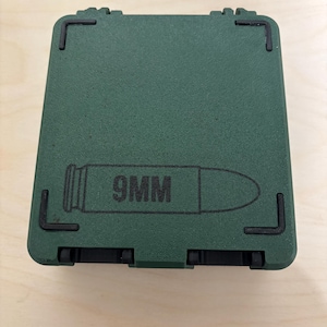 May include: A dark green, rectangular case with a hinged lid and black corner accents. The case features a graphic of a 9mm bullet and the text "9MM" printed in black.