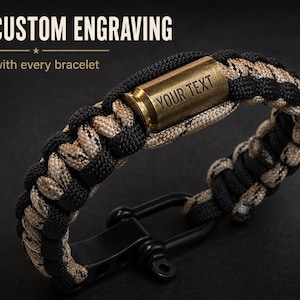 Könnte beinhalten: Ein Paracord-Armband mit einem schwarz-beigen Flechtmuster, einem messingfarbenen Metall-Mittelstück in Patronenhülsenform mit der Gravur YOUR TEXT und einem schwarzen Metall-Schäkelverschluss. Der Text FREE CUSTOM ENGRAVING ist oben zu sehen.