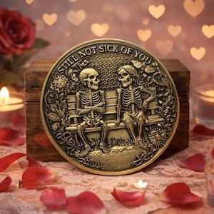 May include: A gold-colored coin with the phrase "STILL NOT SICK OF YOU" encircling a detailed image of two skeletons sitting on a bench. The coin is displayed on a wooden box, surrounded by rose petals and lit candles.