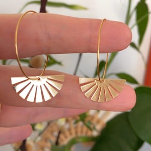 Op de afbeelding: Gouden creolen met een zonnestralenontwerp. De oorbellen zijn gemaakt van dun metaal en hebben een delicate uitstraling.