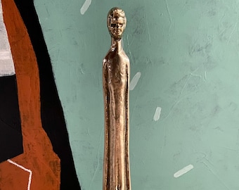 May include: A bronze sculpture of a person standing tall with a minimalist design. The sculpture is a stylized representation of a human figure with a smooth, polished surface.
