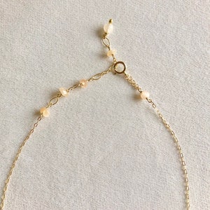 May include: A gold chain necklace with small, light pink beads. The necklace has a lobster clasp closure.