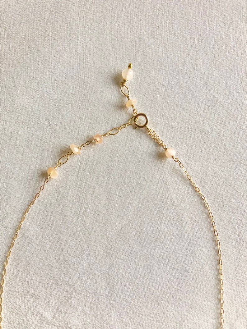 May include: A gold chain necklace with small, light pink beads. The necklace has a lobster clasp closure.