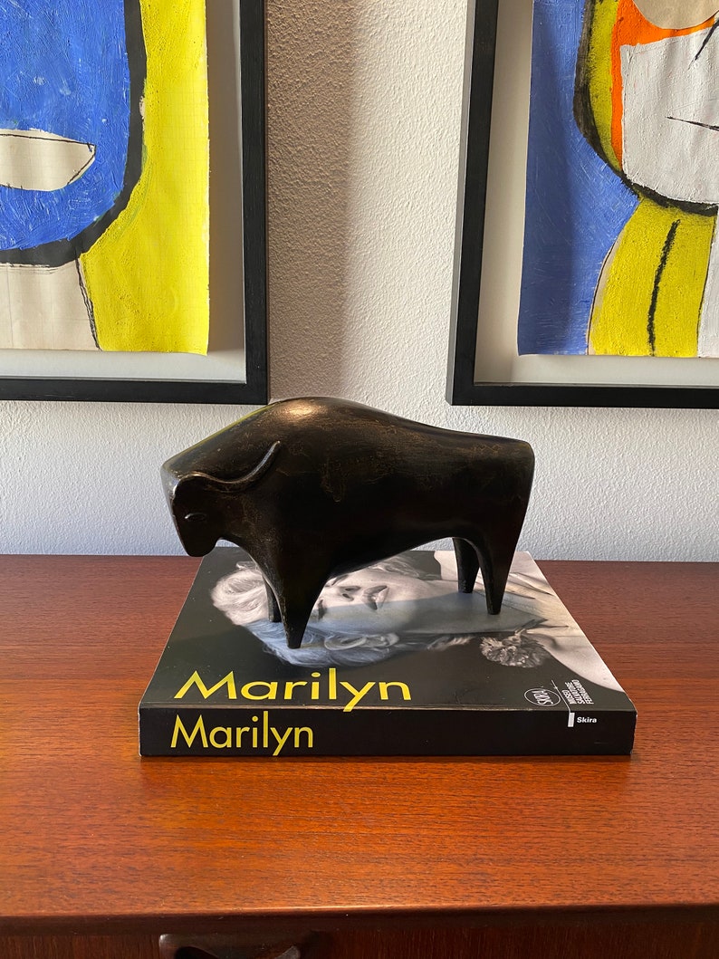 Puede incluir: Una escultura de bronce negra en forma de toro sobre un libro negro con el t&iacute;tulo "Marilyn Marilyn" en letras doradas.