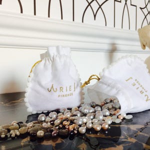 May include: Two white drawstring pouches with gold lettering. The pouches are labelled "Aries Firenze". The pouches are filled with a variety of pearl and gemstone beads.