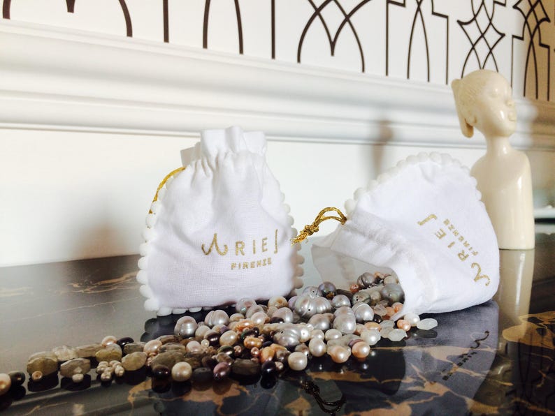May include: Two white drawstring pouches with gold lettering. The pouches are labelled "Aries Firenze". The pouches are filled with a variety of pearl and gemstone beads.
