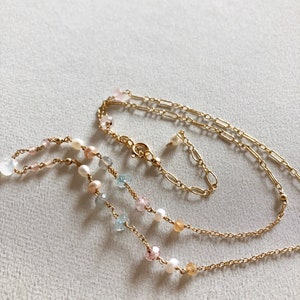 Puede incluir: Un collar de cadena dorada con m&uacute;ltiples hileras de cuentas. Las cuentas son una mezcla de blanco, azul claro, rosa y amarillo.