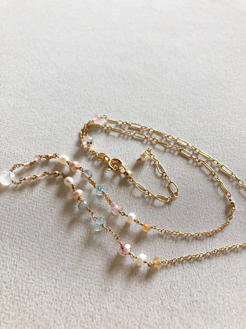 Puede incluir: Un collar de cadena dorada con m&uacute;ltiples hileras de cuentas. Las cuentas son una mezcla de blanco, azul claro, rosa y amarillo.