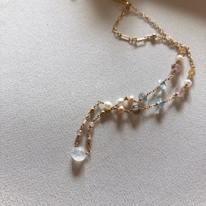 Puede incluir: Un delicado collar de cadena dorada con m&uacute;ltiples hebras que presenta una variedad de cuentas de piedras preciosas, incluyendo perlas, aguamarina y cuarzo rosa.