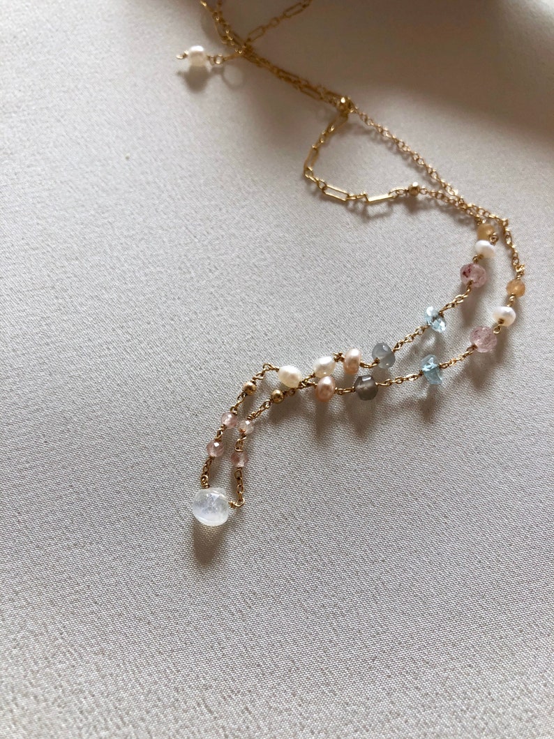 Puede incluir: Un delicado collar de cadena dorada con m&uacute;ltiples hebras que presenta una variedad de cuentas de piedras preciosas, incluyendo perlas, aguamarina y cuarzo rosa.