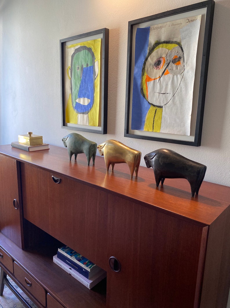 Puede incluir: Un aparador de madera con tres cajones y dos puertas. El aparador est&aacute; decorado con cuatro figuritas de animales de bronce y una peque&ntilde;a caja dorada en la parte superior. Dos pinturas abstractas enmarcadas de rostros est&aacute;n en la pared detr&aacute;s del aparador.