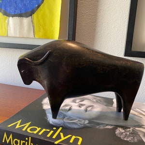 Puede incluir: Una escultura estilizada negra de un toro, de pie sobre un libro titulado "Marilyn Marilyn".