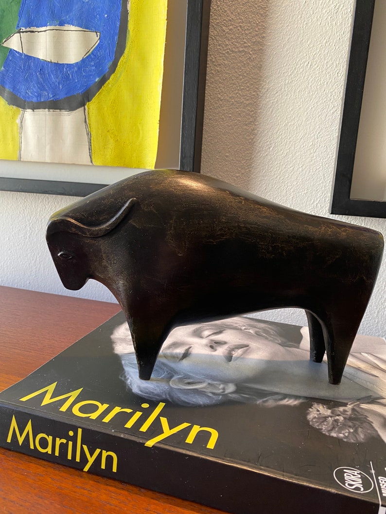 Puede incluir: Una escultura estilizada negra de un toro, de pie sobre un libro titulado "Marilyn Marilyn".