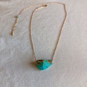 May include: A gold chain necklace with a turquoise gemstone pendant. The pendant is a faceted, geometric shape.