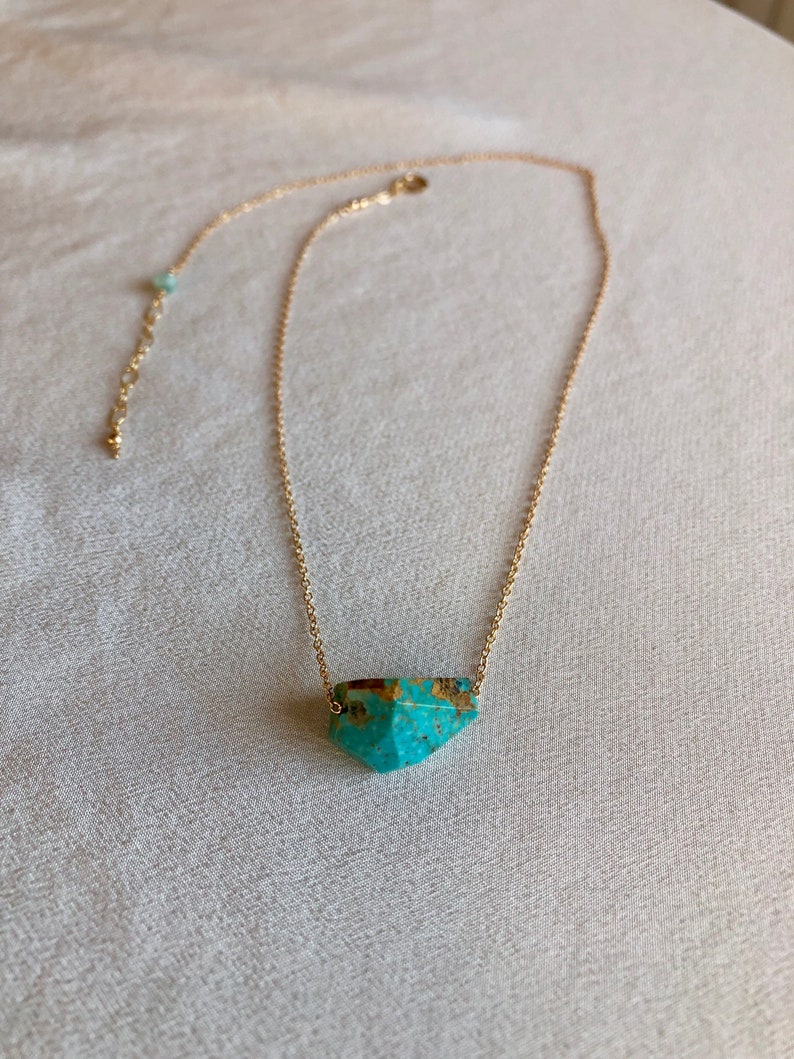 May include: A gold chain necklace with a turquoise gemstone pendant. The pendant is a faceted, geometric shape.