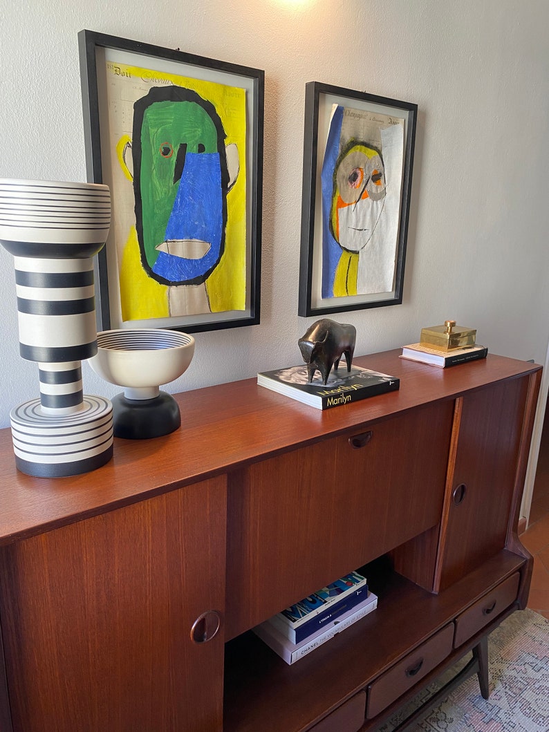 Puede incluir: Un armario de madera con dos puertas y tres cajones. El armario est&aacute; decorado con dos cuadros enmarcados de caras abstractas y una escultura de toro negro. El armario est&aacute; sobre una alfombra con un patr&oacute;n geom&eacute;trico.