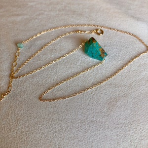 May include: A gold chain necklace with a turquoise stone pendant. The chain is delicate and has a small green stone charm.
