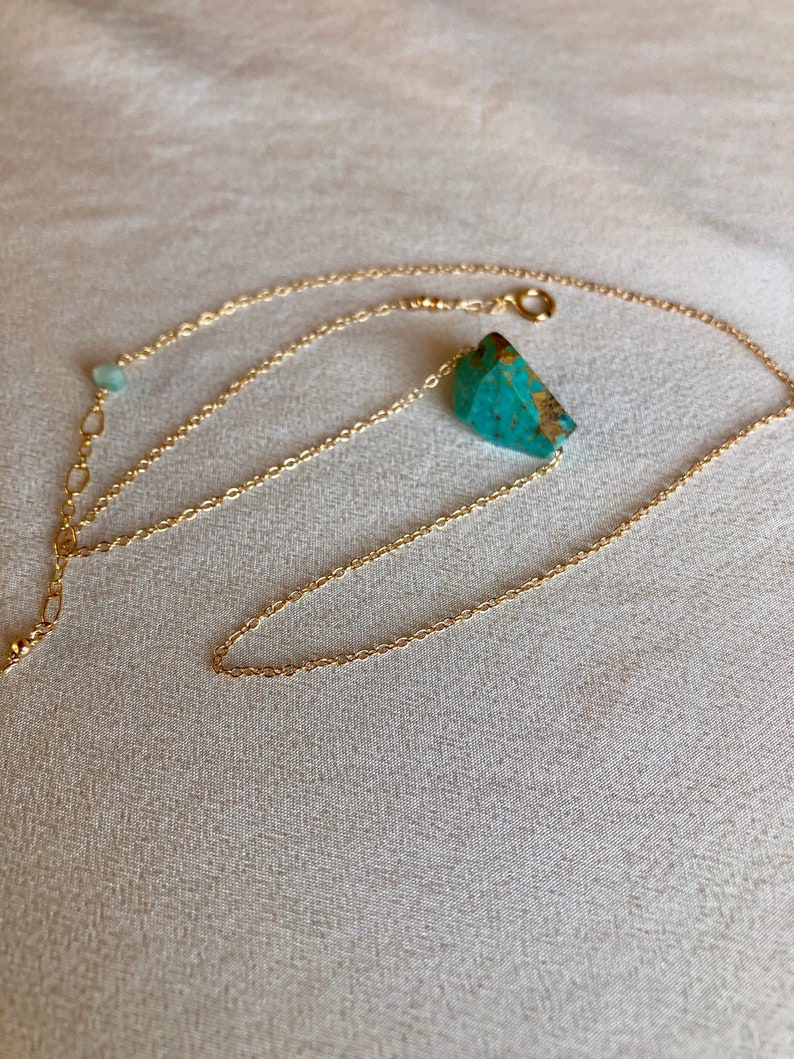 May include: A gold chain necklace with a turquoise stone pendant. The chain is delicate and has a small green stone charm.