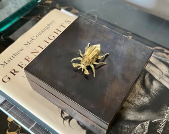 May include: A black wooden box with a gold beetle on the top. The box is sitting on a book titled "Greenlights" by Matthew McConaughey.