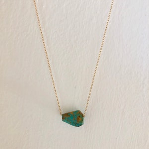 May include: A gold chain necklace with a turquoise gemstone pendant. The pendant is a unique, irregular shape.