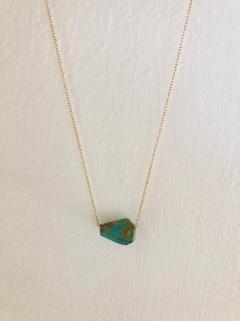 May include: A gold chain necklace with a turquoise gemstone pendant. The pendant is a unique, irregular shape.