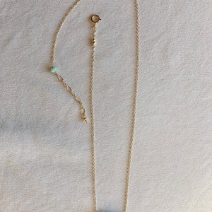 May include: A gold chain necklace with a turquoise stone pendant. The stone is a rough, irregular shape and has a green and brown colour.
