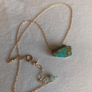 May include: A gold chain necklace with a turquoise gemstone pendant and a smaller green gemstone bead.