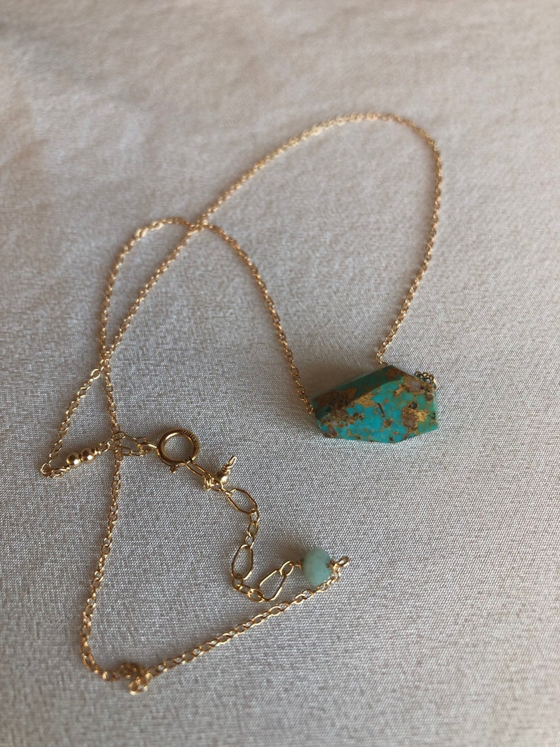 May include: A gold chain necklace with a turquoise gemstone pendant and a smaller green gemstone bead.