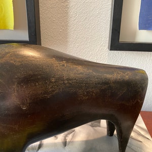 Puede incluir: Una escultura abstracta de cer&aacute;mica de color marr&oacute;n oscuro que representa un toro estilizado con una superficie lisa ligeramente texturizada. La escultura tiene un cuerpo redondeado y cuatro patas.