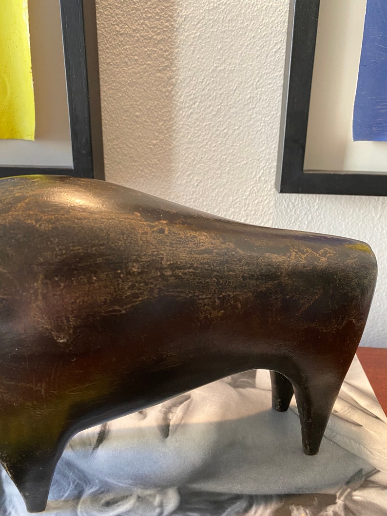 Puede incluir: Una escultura abstracta de cer&aacute;mica de color marr&oacute;n oscuro que representa un toro estilizado con una superficie lisa ligeramente texturizada. La escultura tiene un cuerpo redondeado y cuatro patas.