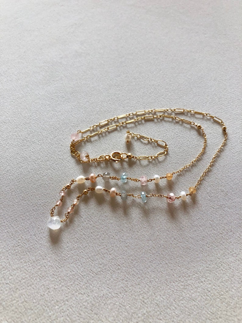 Puede incluir: Un delicado collar de cadena de oro con un dise&ntilde;o en capas. El collar presenta una variedad de peque&ntilde;as piedras preciosas en tonos de rosa, azul y blanco, as&iacute; como peque&ntilde;os acentos de perlas.
