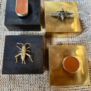 Peut inclure: Quatre boîtes décoratives avec des motifs différents. Deux boîtes sont noires avec des accents en laiton, l'une a un patch en cuir et l'autre un cricket en laiton. Deux boîtes sont dorées avec des accents en laiton, l'une a un patch en cuir et l'autre une abeille en laiton.