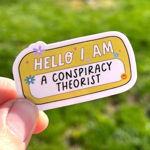 Puede incluir: Pegatina amarilla con texto blanco que dice "Hello I am a conspiracy theorist" con una carita sonriente en la esquina. La pegatina tiene un borde blanco y está decorada con pequeñas flores.