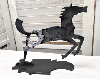 May include: Black metal sculpture of a horse in a running pose. The horse is standing on a black metal base.