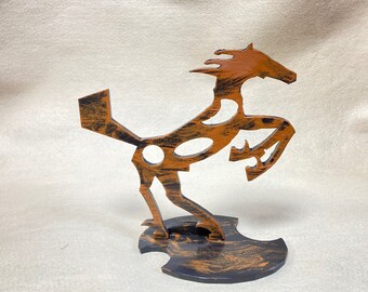 May include: A metal sculpture of a horse in a rearing pose. The horse is painted in shades of orange and black, with a distressed finish. The sculpture is mounted on a black base.