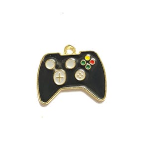 May include: A black enamel video game controller charm with gold trim. The controller has white, red, yellow, and green buttons. The charm has a gold loop at the top for attaching to a necklace or bracelet.