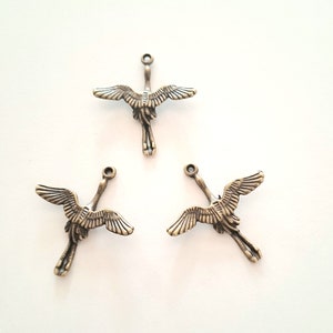May include: Three antique gold-toned metal charms shaped like cranes with outstretched wings.