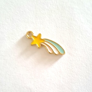 May include: A gold-colored charm in the shape of a shooting star. The star is yellow, with a light blue and pink trail. The charm has a small loop at the top for attaching to a necklace or bracelet.