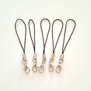 Peut inclure: Cinq breloques de téléphone en cordon noir avec des fermoirs à homard argentés.