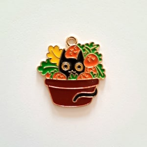 Peut inclure: Un charme en métal doré représentant un chat noir qui sort d'un pot rouge rempli de légumes orange et verts.