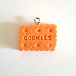 Peut inclure: Breloque en argile polymère orange en forme de biscuit avec le mot "COOKIES" en relief. Le breloque est doté d'un anneau de saut argenté fixé en haut.