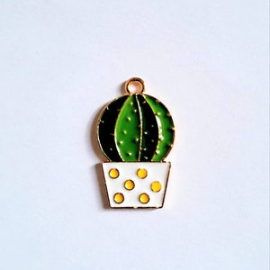 Peut inclure: Un cactus vert avec des points jaunes dans un pot blanc avec un bord doré. Le cactus a une boucle dorée en haut pour l'accrocher.